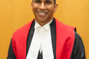Headshot of a male judge wearing black, red and white judicial robes. 
