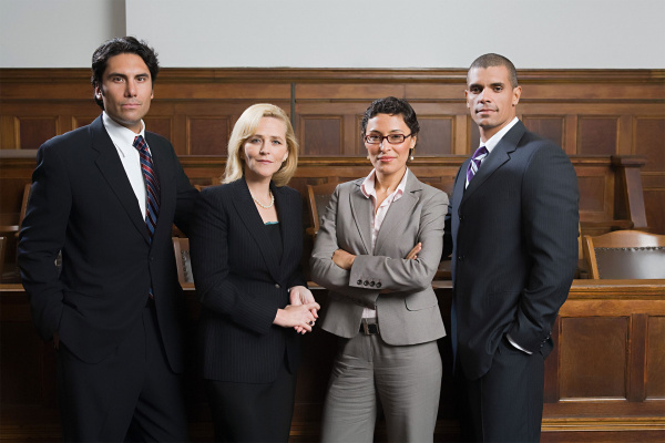 Four legal professionals standing in a courtroom. 