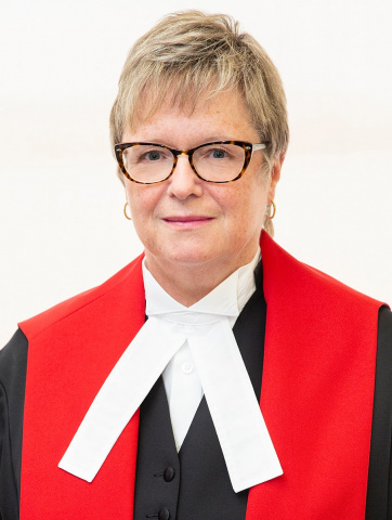 White woman with glasses and short blonde hair wearing red, black and white judicial robes. 