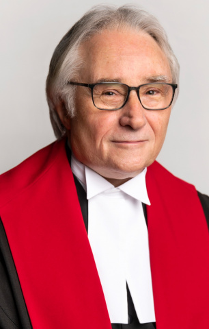 Man with gray hair and glasses in red, black and white judicial robes. 