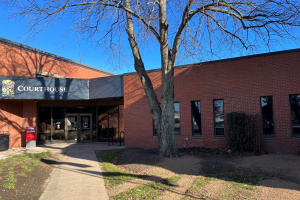 Brick building with a courthouse sign and a tree out front. 