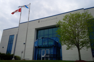 Large white building with glass entrance, a tree and flags flying out front. 