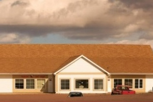 Single story white building with a brown roof and clouds in the sky. 