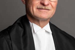 White man with glasses wearing black and white judicial robes.