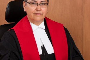 Indigenous woman with glasses and short hair wearing black, red and white judicial robes.