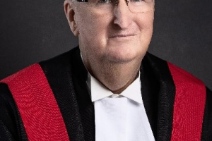 White man wearing glasses and red, black and white judicial robes. 