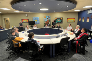 Judges in robes and students sit around a circular table in a courtroom with Indigenous artwork on the walls. 