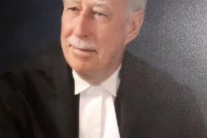 Bald white man with a moustache wearing black and white judicial robes. 